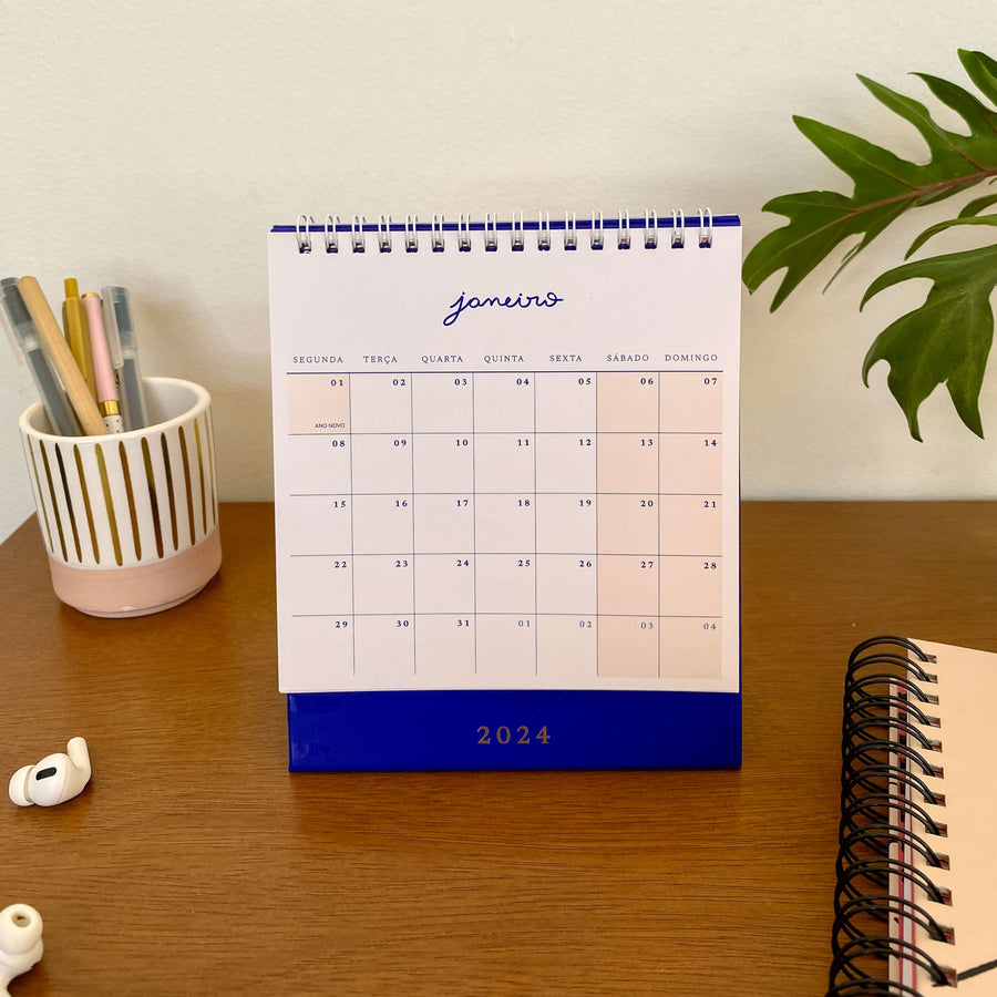 calendário de mesa 2024 azul royal sobre mesa de trabalho com caneteiro e plantinha no fundo