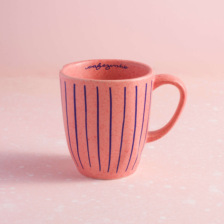 caneca rosa com listras azuis e a palavra cafezinho dentro sobre fundo rosa claro