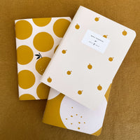 trio de cadernos costurados com estampa de tangerina sobre tecido amarelo mostarda
