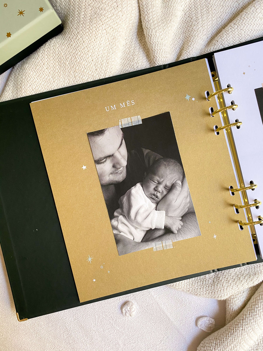 livro do bebê sobre cama com foto de bebê no colo do pai na página um mês