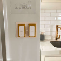 blocos de geladeira presos em porta de geladeira. ao fundo é possível ver uma pia com torneira dourada e acabamentos em branco