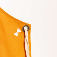 detalhe do ilhós do avental de algodão mostarda com estampa de macarrão gravatinha